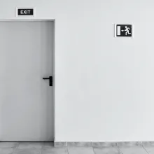 A white door with an exit sign above it and an exit symbol beside it.