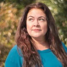 Headshot depicts Miroslava Gonzalez, a storyteller, community advocate, Producer, Writer and Director. She has long brown hair, green eyes and is wearing a teal-colored sweater.