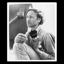 A black-and-white photo of a man holding a camera lens. 