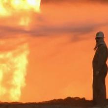 A person looks at a fire on the horizon, from Werner Herzog and Paul Berriff's 'Les­sons of Darkness.'