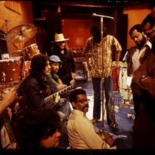 Ellis Haizlip, sits in the middle of the set of his variety show 'SOUL' surrounded by members of the '70s funk band Mandrill, some members of whom are holding their instruments.