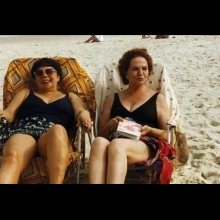 Two older women smile while sitting in beach chairs near the ocean, from Heddy Honigmann's 'Amor Natural'.