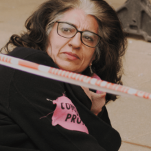 A woman protestor, with shoulder-length brown hair, dressed in black and wearing glasses, is sitting on the ground looking over her shoulder. From Maia Kenworthy & Elena Sanchez Bellot's “Rebellion.” Photo courtesy of DOK Leipzig. 