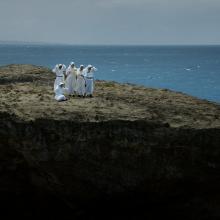 Seis monjas con sus hábitos blancos de pie en tierra, el océano a su alrededor. Del filme 'Landfall' por Cecilia Aldarondo. Cortesía de Cecilia Aldarondo