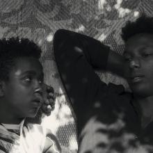 Black and white photo of two young Black men lying on a mat. (l. to r.) Mohammed Arif and Ibrahim Mohammed, two boys from Harar, Ethiopia, as seen in Faya Dayi, directed by Jessica Beshir. Courtesy of Merkhana Films.