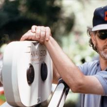 Steven Spielberg leans on a Panavision camera. 