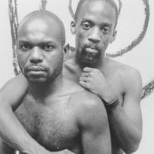 Two Black men embrace each other. Marlon Riggs' 'Tongues United' is looked at as an exploration of regional exile in tandem with personal exile in 'Between the Sheets, in the Streets Queer, Lesbian, Gay Documentary'.