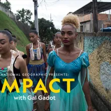 A group of medium- and dark-skinned dancers are walking through an alley on a hill in their performance outfits