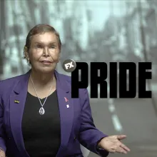 Elder adult with medium skin tone, short ash blonde hair, wearing a purple blazer over a black tee.