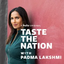 Padma Lakshmi is an Indian woman with straight dark brown hair, wearing a pine green denim jacket, standing against a pink wall