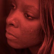 A close up shot of a Black woman with long brown hair looking off screen. A still from 'Woman on the Outside.'