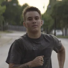 A man with white skin and short blond hair runs down a street.