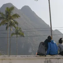 Three people sit on a ledge and stair at a mountain.