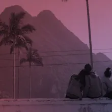 Three people sit on a ledge and stair at a mountain.