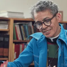 A older Black person with gray hair wearing a blue coat.