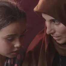 A woman in a brown hijab talks to a little girl.