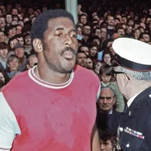 Clyde Best walks through the pitch at West Ham United, with a sea of fans in the stands behind him