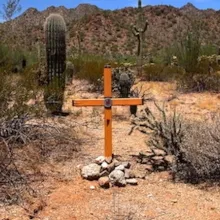 An artistic orange cross propped up with stones in the Sonoran Desert