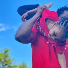 Black father holds smiling child upside down in playful manner