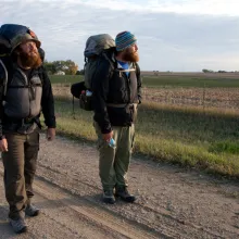 two veterans pause in the middle of road amid their backpacking trip