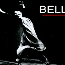 Black and white photo of female dancer in a white flowing dress with her arms raised in the air