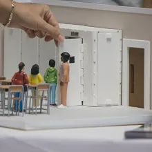 hand of person uses small replica of school classroom to teach gun related safety protocols