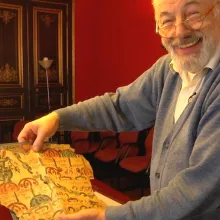 A Caucasian man is holding up an ancient scroll while smiling.