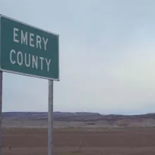 A large empty vista with a single green highway sign reading "Emery County"