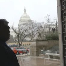A man is in the shadows standing at the doorway with the US State Capital across the street