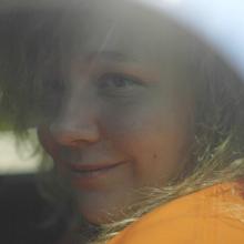 A still from "United States vs. Reality Winner": A young woman with blonde hair and an orange sweatshirt looks out from the window of a car.