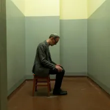 A man sitting in an empty small room looking down at his feet