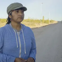 An indigenous woman stands in the shadow of the US-Mexico Border Wall