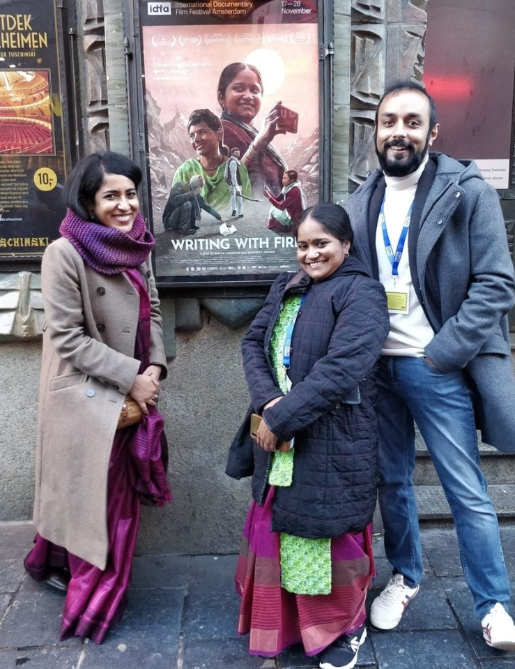 Three smiling people stand in front of a movie poster.