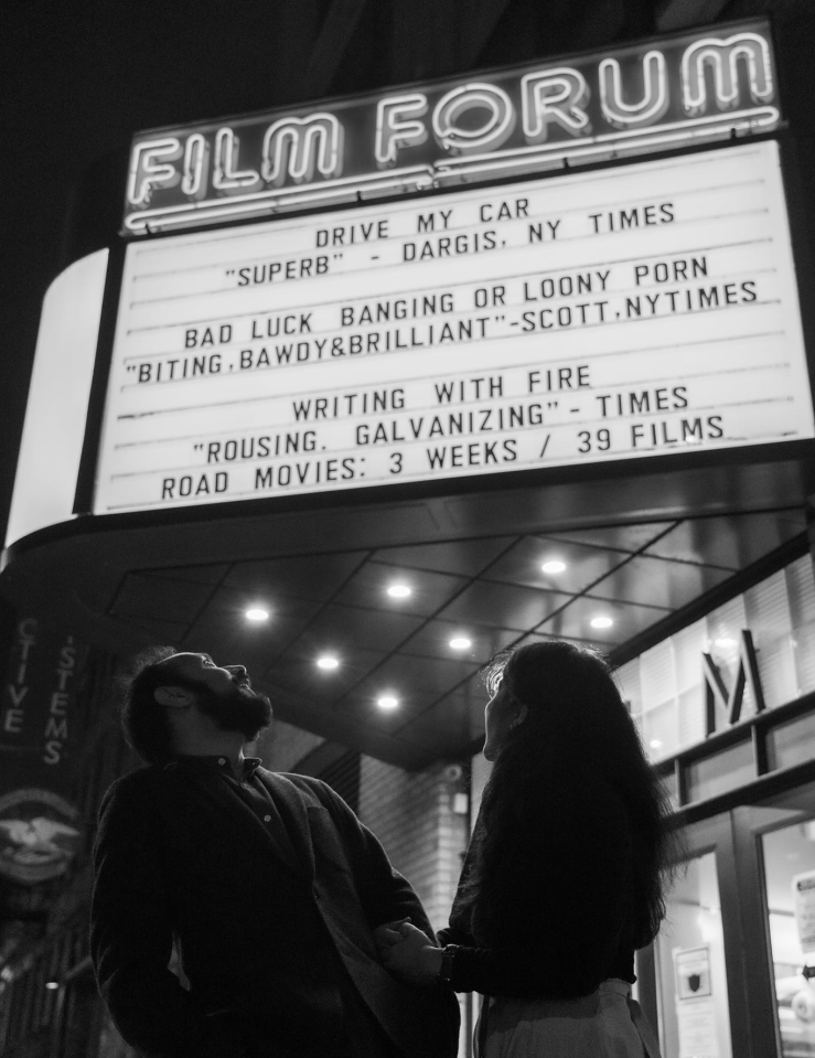 Two people stand below a theater marquee.