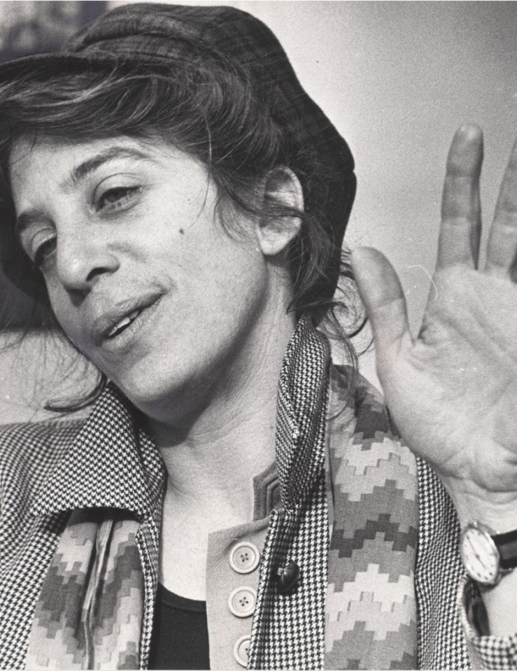 Black and white photo of a white woman with dark hair pulled back under a hat, wearing a scarf and a coat