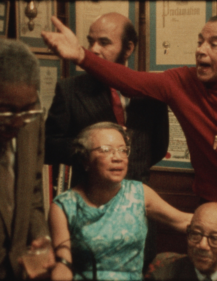 Grainy photo of a group of older Black men and women arguing in a living room