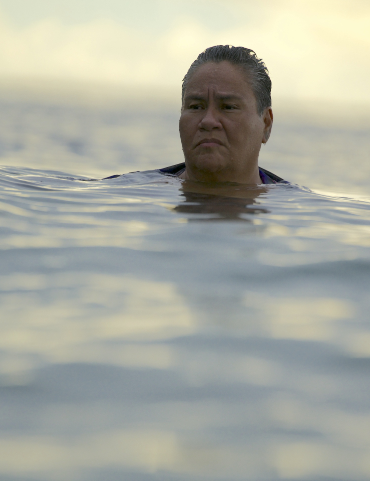 A brown, heavy-set woman's head is seen above ocean water against a sunny sky behind her
