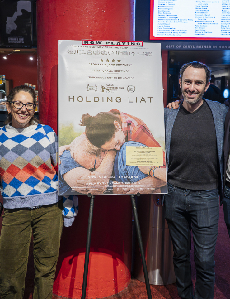 Around a poster of Holding Liat at a movie theater lobby stand two men to the right and two women on the left.