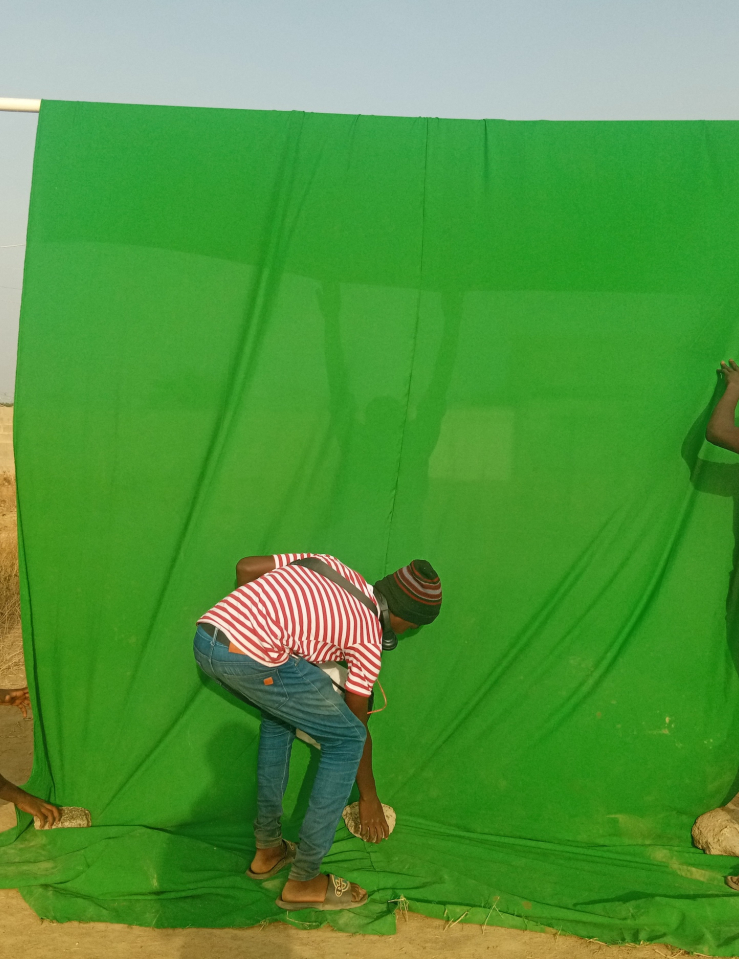 Five young Black kids in jeans and colorful shirts set up a green screen in the middle of a desert field