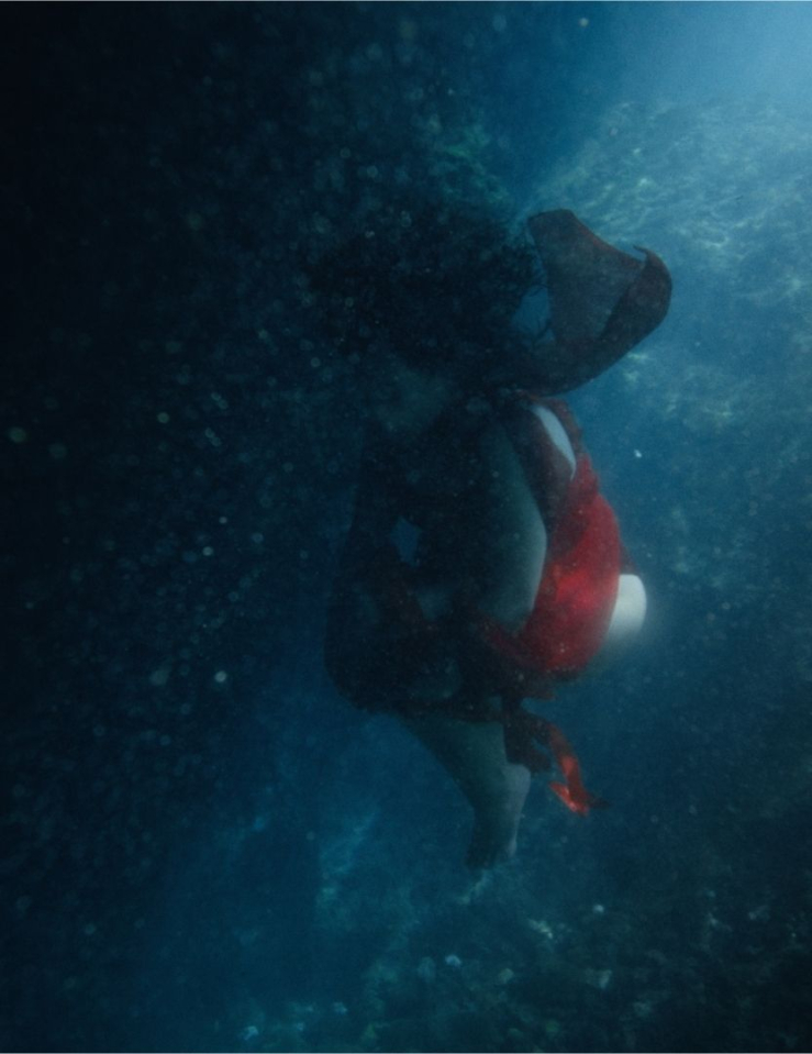 Dark shot of a woman in a red dress floating underwater, her black hair curling up