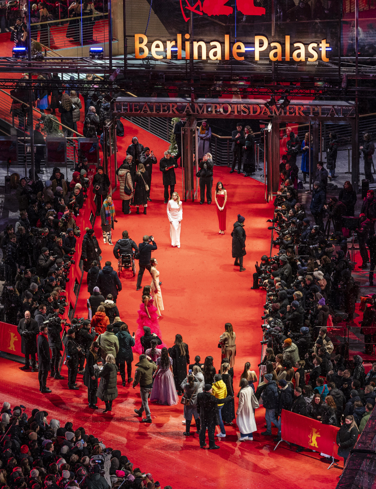 Outdoor, nighttime shot of a red carpet at the Berlinale Palast where photographers crowd folks dressed up near them