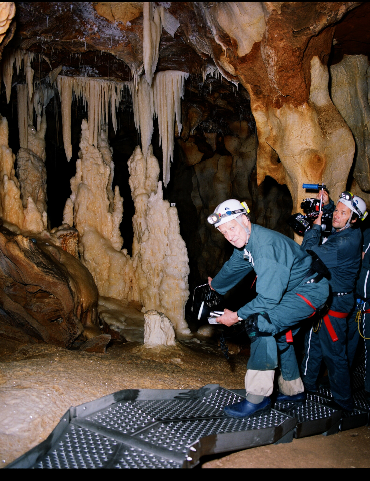 Three middle-aged white men in gear and holding cameras pose for a photo inside a cave lit only by the flash of the camera