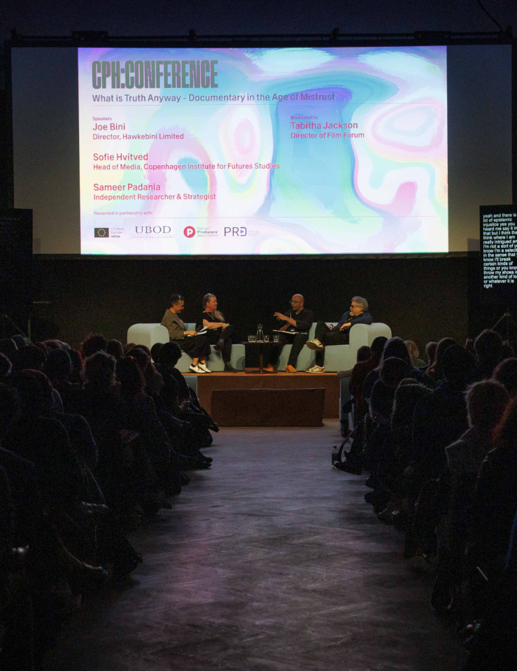 A packed theater with a screen announcing a CPH:DOX panel features four people seated at a stage holding mics mid-conversation