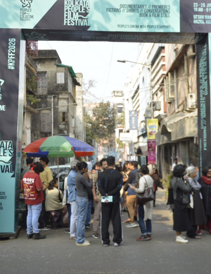 Wide shot of an open street adorned with Kolkata People's Festival banners with various people milling around