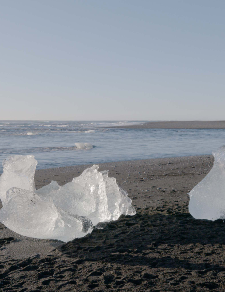Two pieces of ice are seen melting on a sandy beach