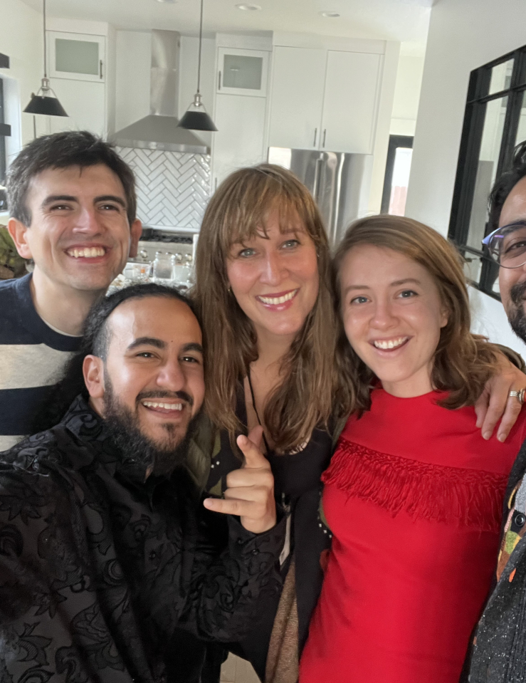 A selfie of three men and two women, all smiling and dressed nicely, taken in a spacious, white kitchen