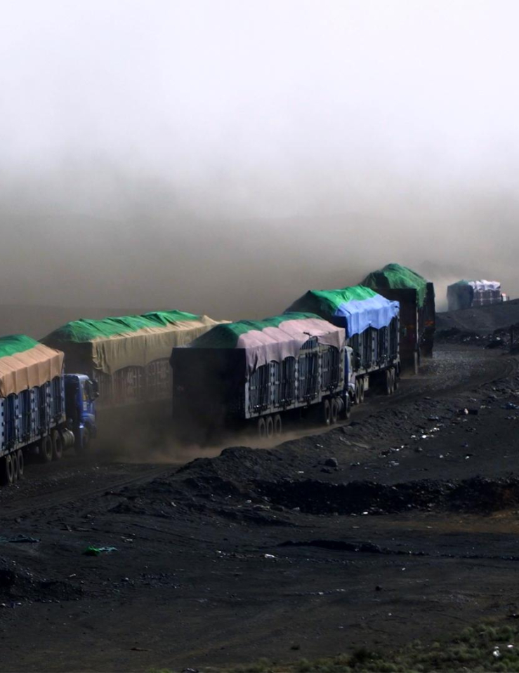 A line of covered trucks drive over black terrain