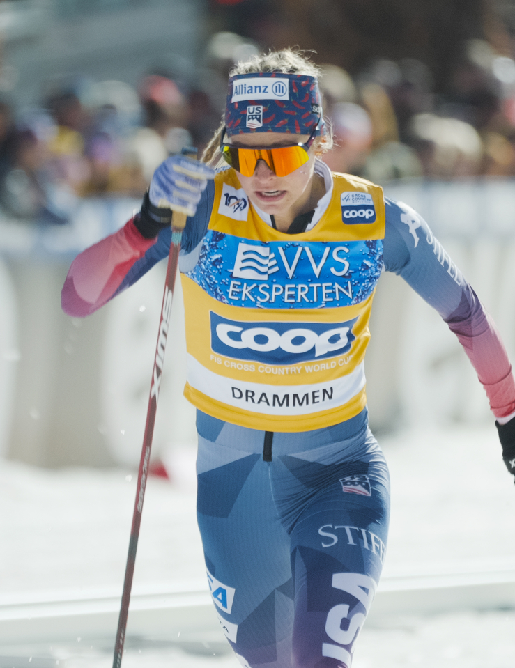 A blonde woman in a ski uniform, goggles, and headband skis furiously