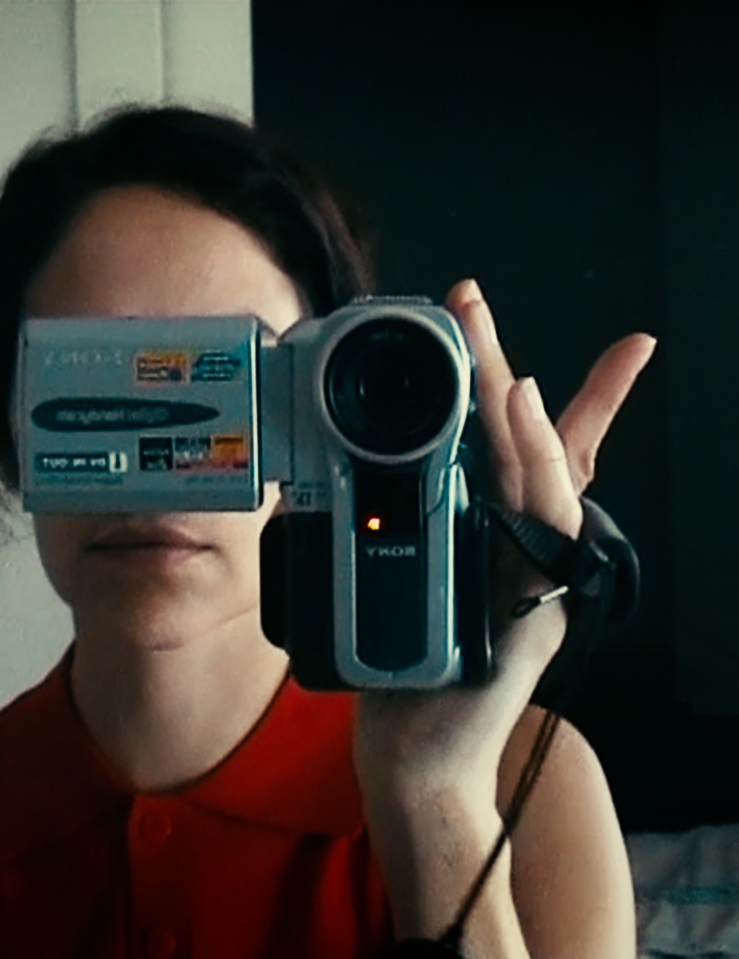 A reflection of a woman in a red, sleeveless top holding a Sony camcorder in front of her face