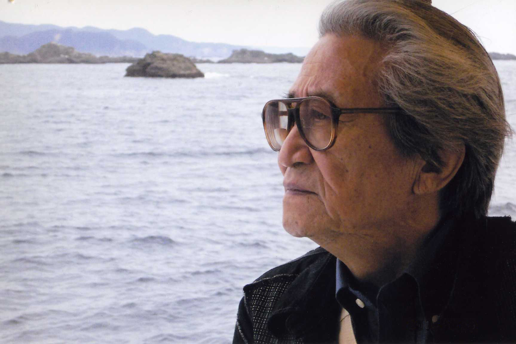 Noriaki Tsuchimoto, a Japanese man wearing glasses, stares out into the ocean. Photo courtesy of Motoko Tsuchimoto.